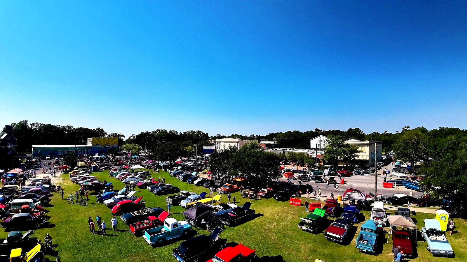 Aerial view of classic cars parked across the riverfront green