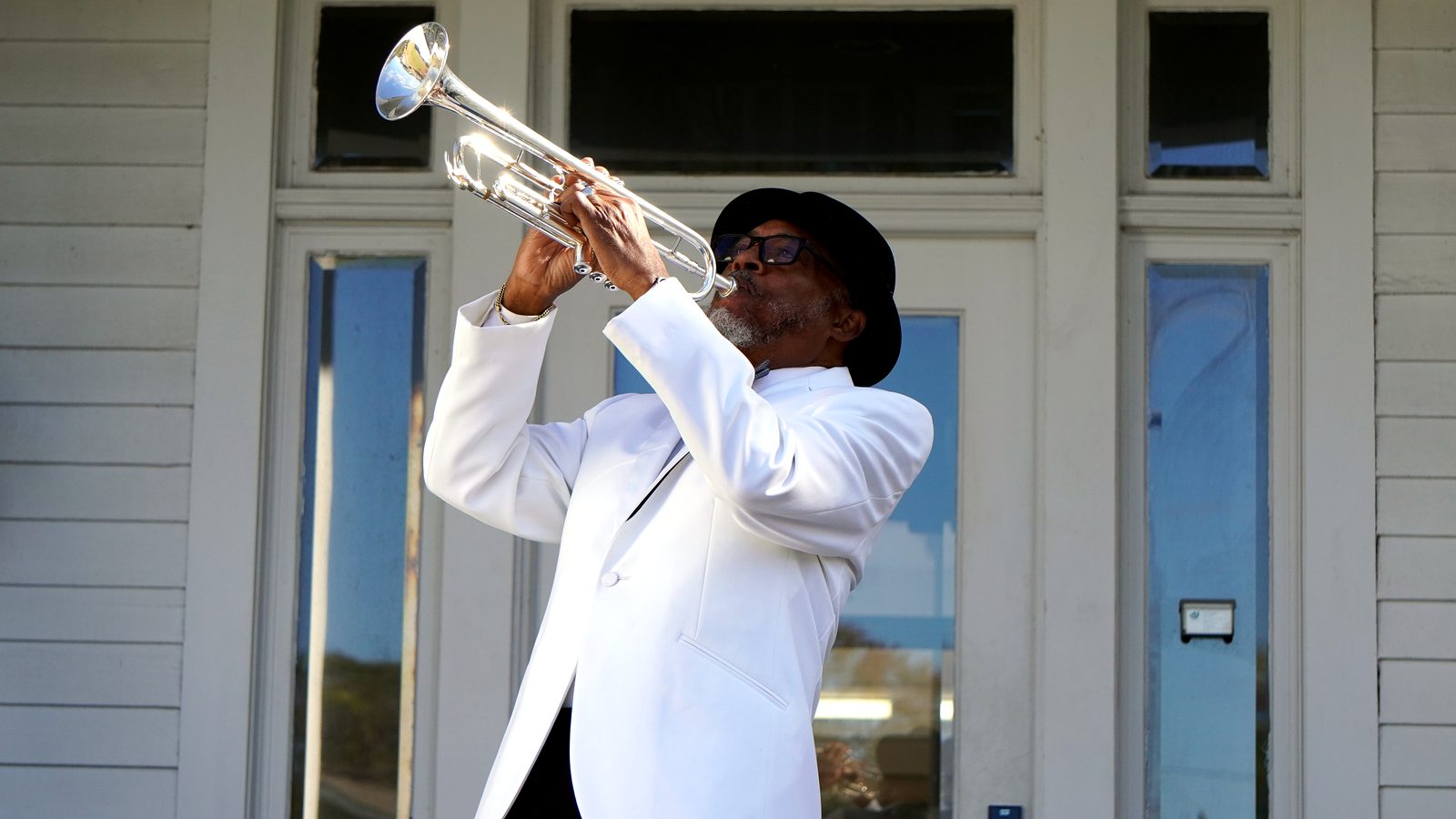 A trumpeter in a white dinner jacket raising his horn on the porch